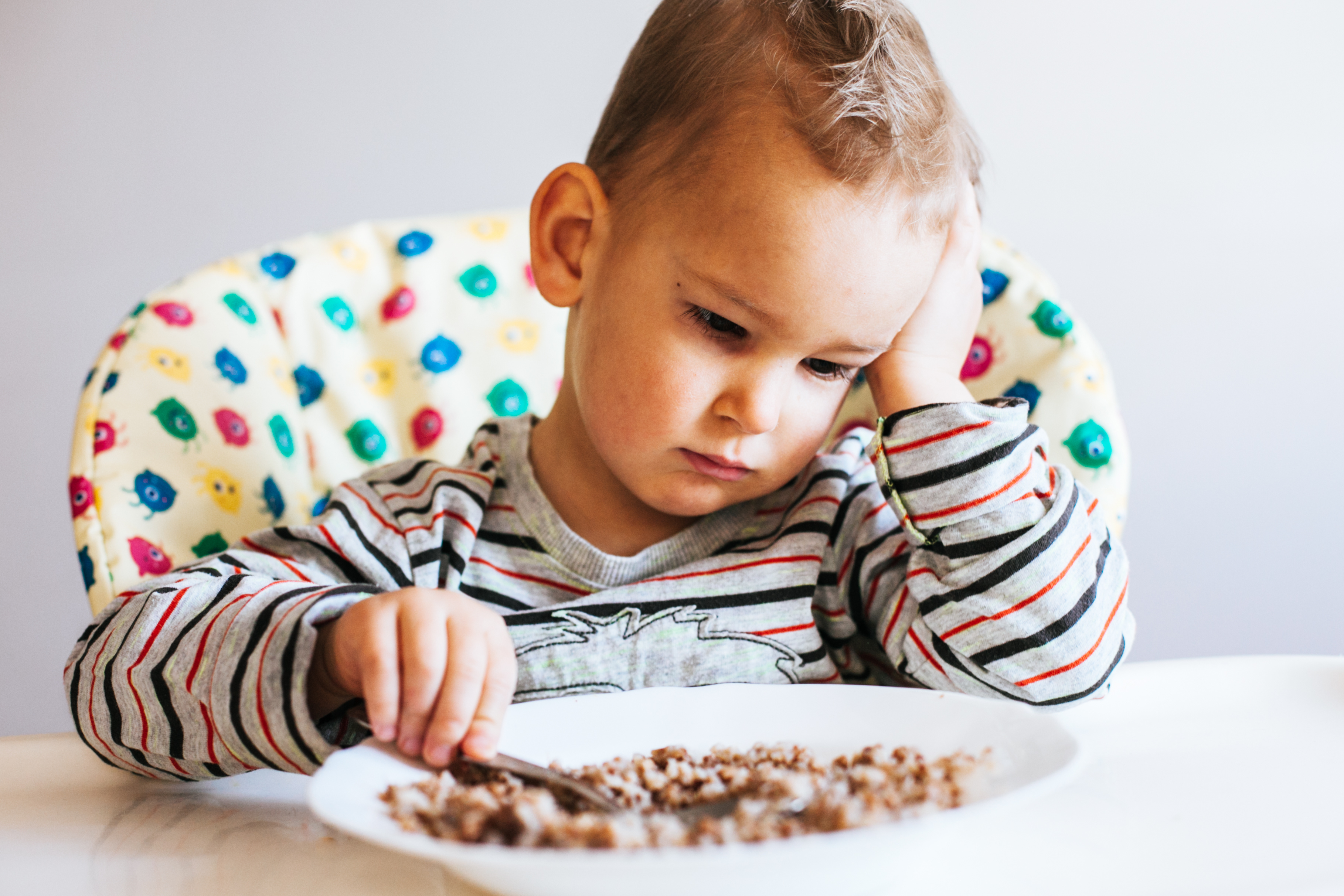 Sitzendes Kleinkind stochert lustlos in seinem Müsli herum.